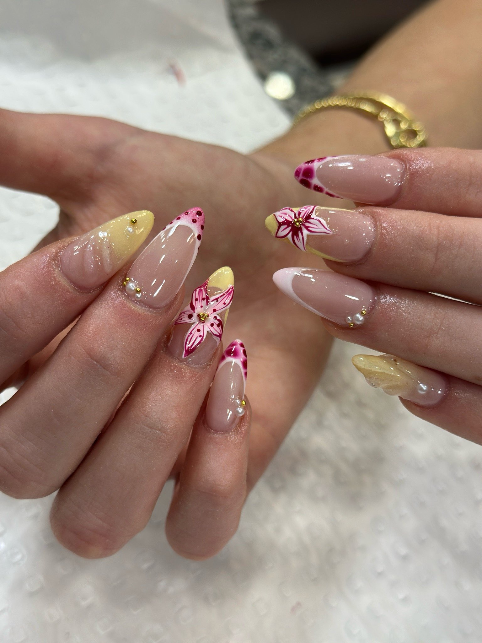 Almond nails with hand-painted pink lilies, yellow tips, pearls and gold studs