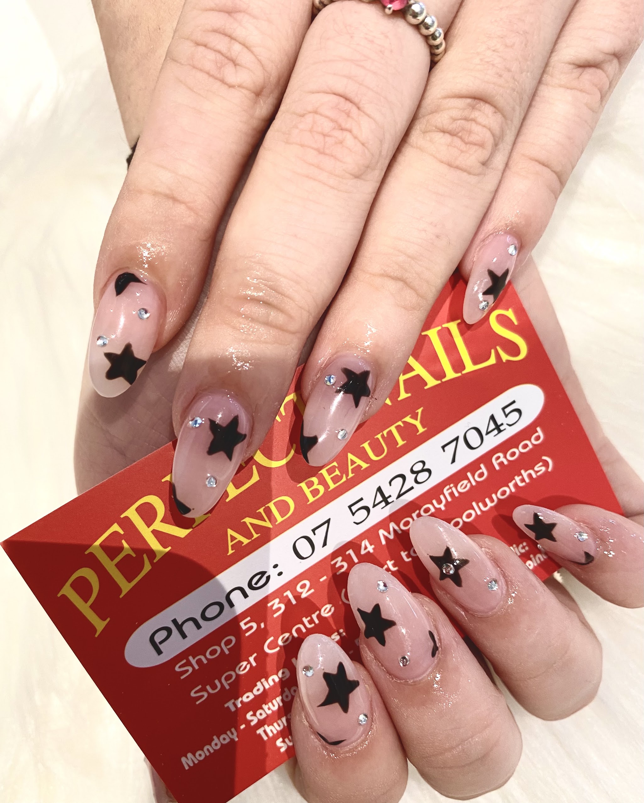 Nude almond nails with black star art and rhinestones