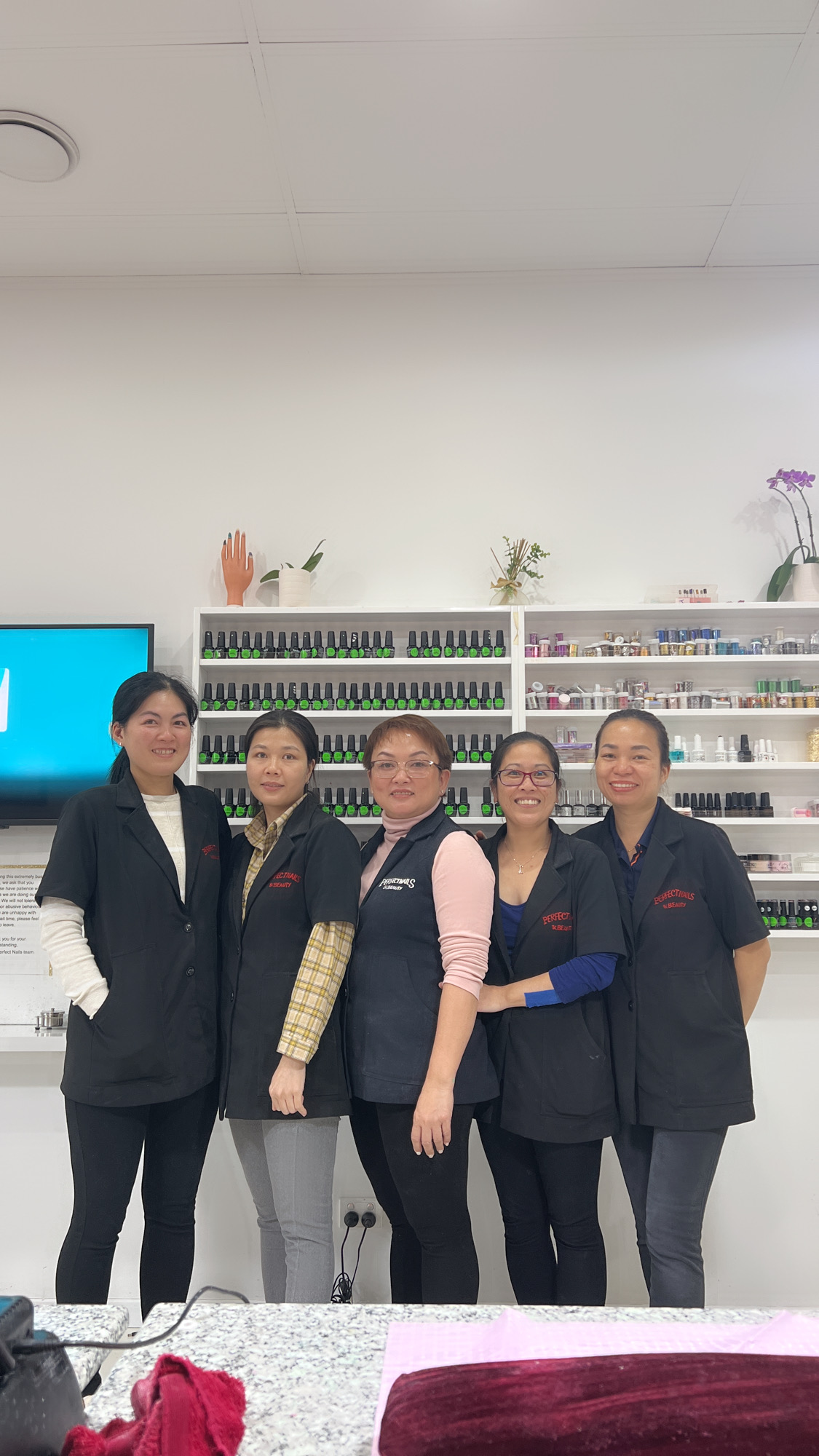 The five-person Perfect Nails and Beauty team in matching jackets in front of the polish wall